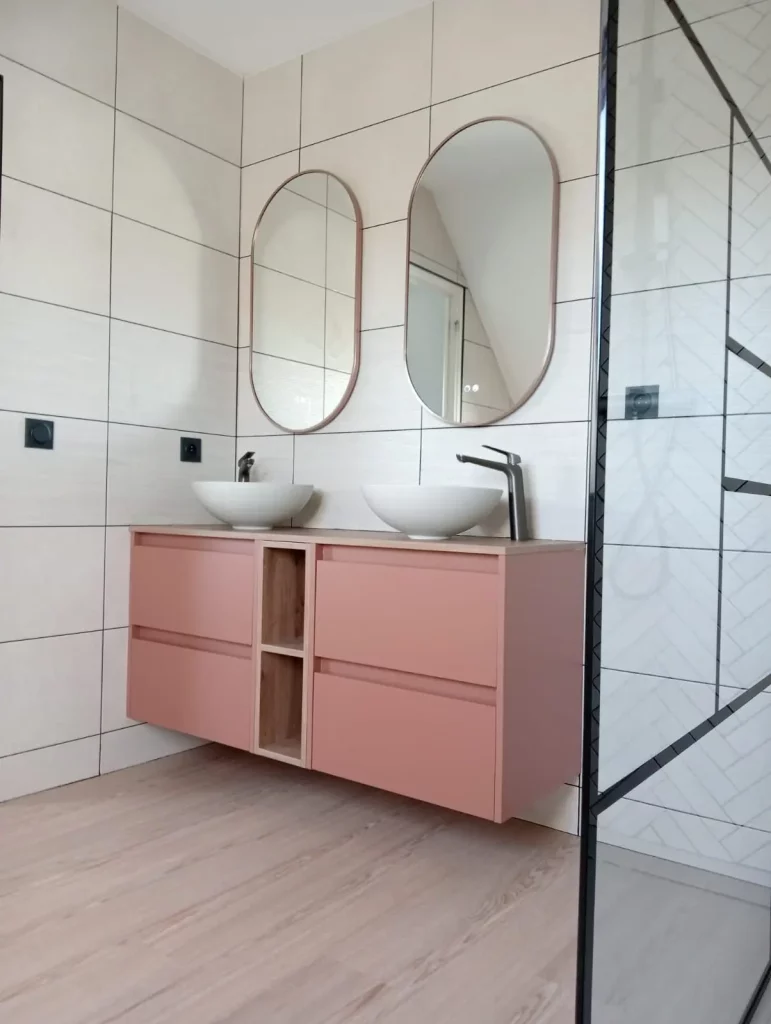 Une salle de bains avec un meuble rose et des miroirs ovales / A bathroom with pink cabinets and mirrors.